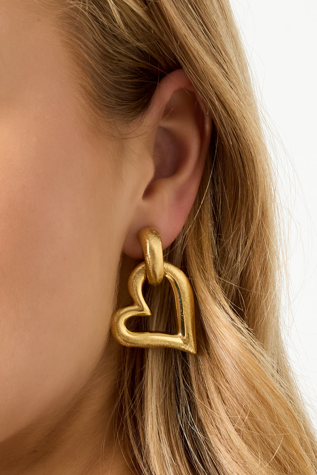 Gold heart drop earrings with a brushed finish, worn by a model.