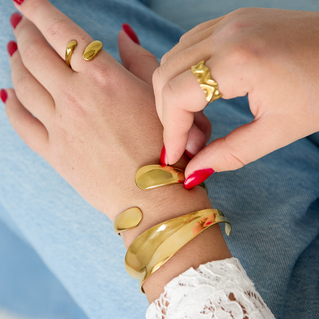 Gold irregular cuff bracelet on a woman's wrist, paired with a matching ring.