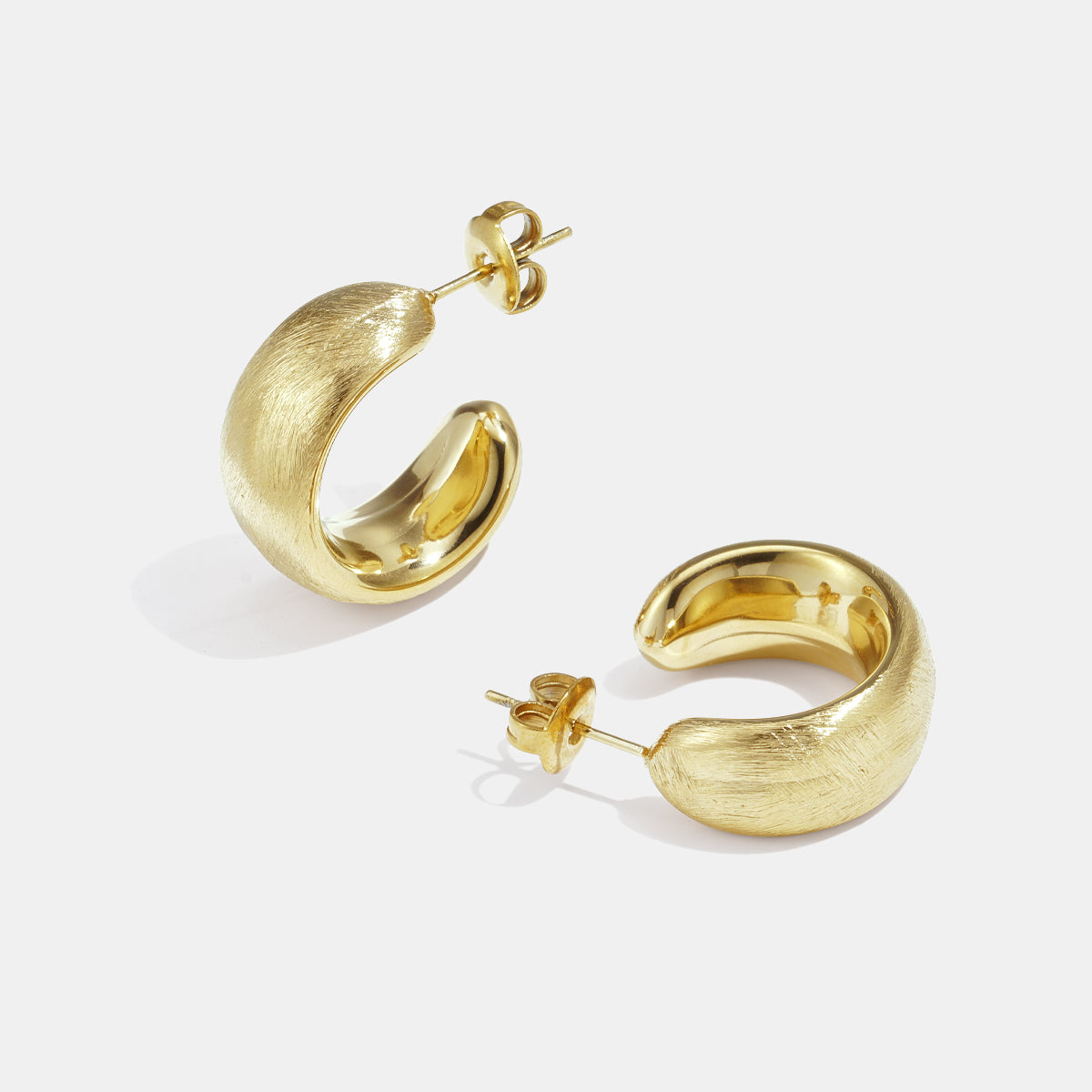 A pair of brushed gold hoop earrings with a subtle sheen, displayed on a white background.