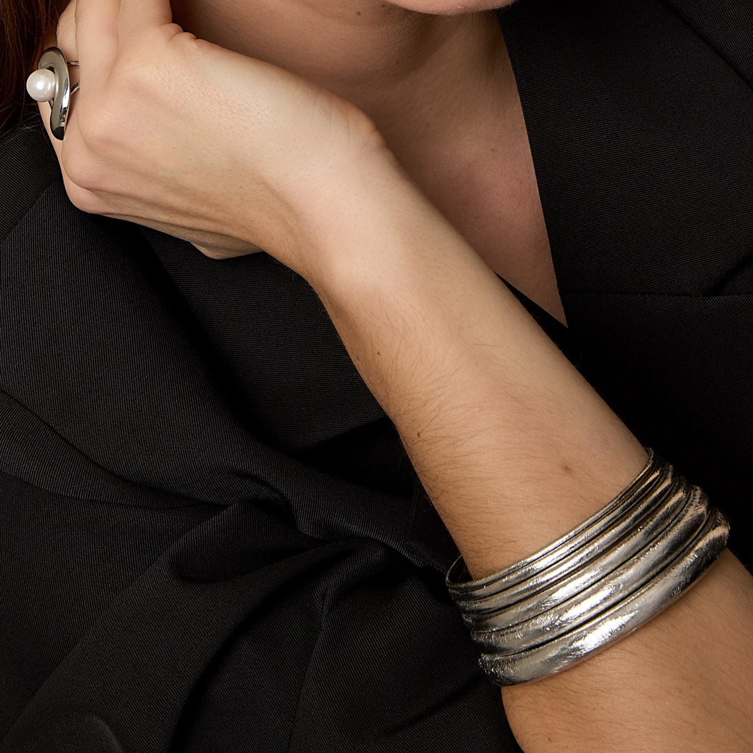 Close-up of a woman's arm wearing a stack of five brushed silver bangles.