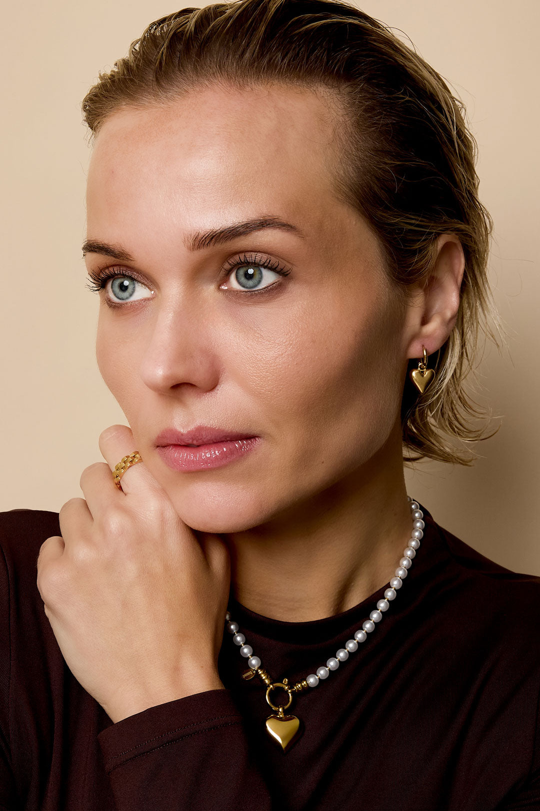 Gold heart drop earrings on a woman with a pearl necklace and gold ring.